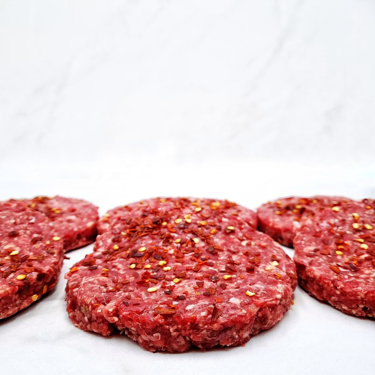 Seasoned burger preparations arranged on a pale surface
