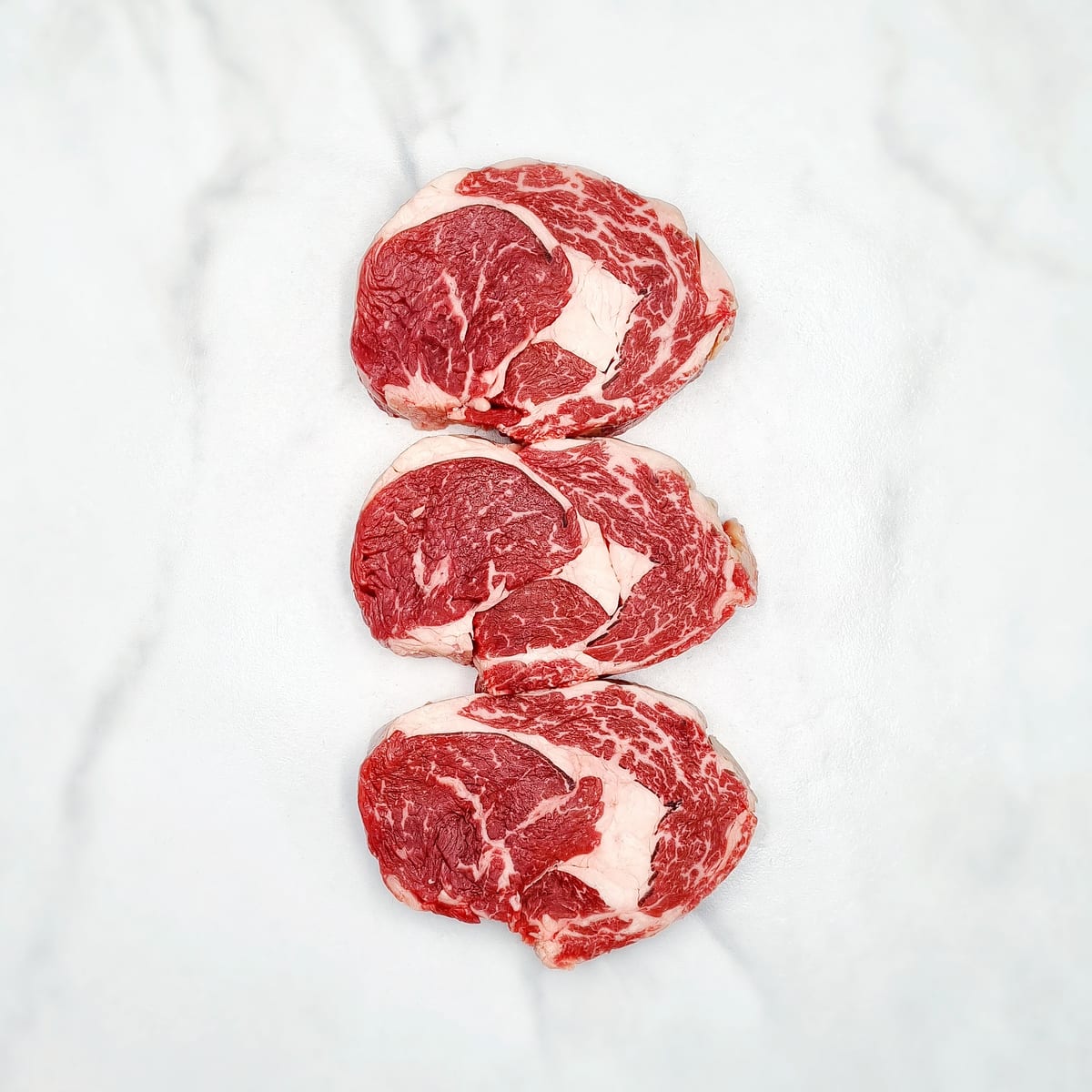 Three marbled steaks arranged on a pale surface